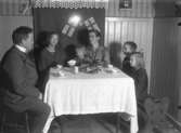 Rumsinteriör, familjegrupp sex personer vid bordet.
Familjen Bäckman: föräldrarna Edit och Johannes Natanael Bäckman, dottern Nanna till vänster.