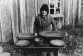 En kvinna vid bord med husgeråd.
Matilda Karlsson.
Trösslingstorp.