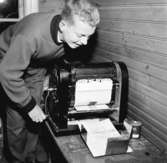En ung pojke arbetar vid kopieringsapparaten med att trycka tidningen Hakarpsbladet.
