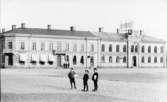 Kvarteret Rådhuset åt torget i Varberg, med hörnet Torggatan-Drottninggatan till vänster. I byggnaden ligger Albert Nelsons manufakturaffär och Dan Lundgrens läderfabrik. I Rådhuset längst till höger finns kongl. telegraf- och rikstelefonstationen inrymd. Fototid: 1910-tal.