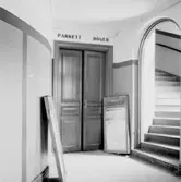 Örebro teater den 27 april 1937. En bild från teaterfoajén (förrummet) som man passerar innan man kommer in i teatersalongen. Dörren rakt fram leder till parkettplatserna på teatersalongens golv, och trappan till höger leder upp till teaterläktarna. De nedmonterade annonstavlorna vittnar om att teatern nyligen har stängts; nämligen år 1936 p.g.a. ekonomiska svårigheter.