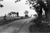 Kyrkan sedd från vägen, 1900-talets första hälft. Ännu löper stenmurarna längs vägen och ett mjölkbord skymtar.