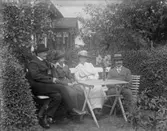 Grupp fyra personer vid ett bord i trädgården.Bostadshus i bakgrunden.