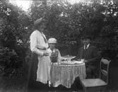 Tre personer vid kaffebordet i trädgården.