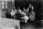 Kaffebjudning utomhus, sju personer vid bordet. Bostadshus i bakgrunden.
Hos Olsson i Hagalund. Från höger bl.a. familjen Hammar.