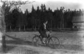 En flicka på cykel. Bostadshus till höger på bilden.
Thea Elfrida Olsson, Erik Theon Olssons dotter.