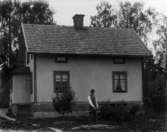 Bostadshus, en man.
Alfred Johansson vid brunnen bakom sitt hus.
