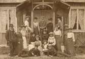 Gruppfoto exteriör, män, kvinnor och barn framför veranda, på verandan hänger unionsflaggor, troligtvis före 1910.