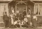 Gruppfoto exteriör, män, kvinnor och barn framför veranda, på verandan hänger unionsflaggor, troligtvis före 1910.
