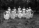 9 flickor i likadana klädningar, utomhus. En dansgrupp. Balett?