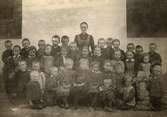 Skolklass ca 30  små barn med lärarinna, flera av barnen har träskor,  troligtvis början 1900-talet, 10930.