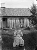 Kvinnoporträtt. En kvinna fotograferad sittande framför ett hus. Exteriör.