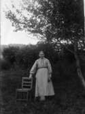 Kvinnoporträtt. En kvinna fotograferad stående utomhus bredvid en stol.