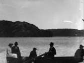 Utflykt. Roddbåt mked passagerare på sjö med berg i bakgrunden.