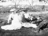 Grupp av män och kvinnor dricker kaffe ute sittande på marken. Mannen som ligger till höger i bild är fotografens farbror, August Sikén.