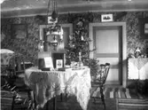 Interiör från ett julprytt rum med ett runt, dukförsett bord i förgrunden. Mellan de två spegeldörrarna står en julgran. Troligen i Klas Sikéns hem, Höjder Karl Gustav, bror till fotografen. 
(Se även bild E6862)