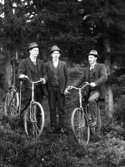 Två män med varsin cykel och en utan, fotograferade i en skogsbacke.