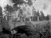 Två kvinnor stående på en bro över ett vattendrag. (Bron kan vara Ryds valvbro. Revs 1967?).