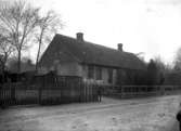 Hus med liten trädgård och uthus, en pojke står framför huset, ”vy 1920” på asken
	Kraftig metallutfällning.