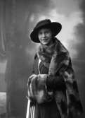 Ateljébild, kvinna med hatt, pälsstola och muff, ”1915 B” på asken
	Metallutfällning.