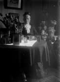 Äldre kvinna vid ett bord med blommor och fotografier 1919
	Blekt.