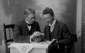 Ateljébild, två läsande män ”vy 1917 J” på asken
	Metallutfällning, värma/väta skada i ena kanten.