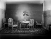 Ateljébild, möbelgrupp, bord, stolar och pallar. Johnsons privata bilder.
	Metallutfällning.