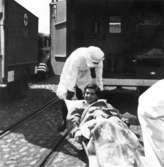 En ung kvinna som varit fånge i Bergen-Belsen anländer till Kalmar med skeppet Prins Carl och lyfts ombord på en lastbil. Observera mottagarnas andningsskydd! Många patienter hade tyfus och TBC.