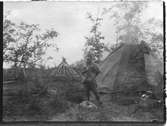 John Bauers Lapplandsresa sommaren 1904. Ett sameläger i Ripainenjoki. En man står framför en kåta.