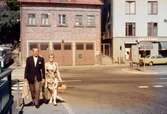 En kvinna och en man vid Gamla Torget i Mölndal, 1970-tal. I bakgrunden ses huset Kvarnbygatan 41, tidigare brandstation och garage för polisbilar, numera Mölndals målarskola. Till höger ses liten del av huset Kvarnbygatan 43, tidigare Mölndals stadshus, sedermera musikskola. Vy från Forsebron.

För mer information om bilden se under tilläggsinformation.