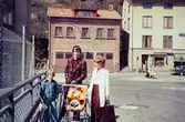 En kvinna, en man och två barn, det ena i barnvagn, står på Forsebron i Mölndal, 1970-tal. I bakgrunden till vänster ses del av gaveln till huset Kvarnbygatan 4. I mitten ses Kvarnbygatan 41, tidigare brandstation och garage för polisbilar, numera Mölndals målarskola. Till höger ses del av huset Kvarnbygatan 43, tidigare Mölndals stadshus, sedermera musikskola.

För mer information om bilden se under tilläggsinformation.