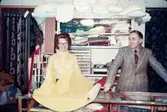 En kvinna och en man fotograferade i en tygaffär, troligtvis vid eller i närheten av Gamla Torget i Mölndal, 1970-tal.

För mer information om bilden se under tilläggsinformation.