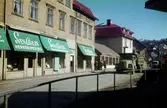 Vy från Papyrus port mot byggnader vid Kvarnbygatan i Mölndal, 1960-1970-tal. Närmast ses från vänster Sven Ahlin Herrekipering med adress Kvarnbygatan 25 och C.J. Johanssons Järnhandel med adress Kvarnbygatan 27.

För mer information om bilden se under tilläggsinformation.