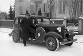 Herre med Chevrolet på en bild från 1934. Bilen kommer troligen från Geijers Motoraffär, agent för GM i Karlstad. Bilden togs på Museigatan som då fortfarande hade kvar sitt gamla namn Älvgatan.