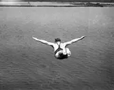 Bildserie från slutet av 1930-talet från Karlstads dåvarande simstadion. Anläggningen låg i anslutning till den s k badholmens östra sida söder om Kanikenäset. Badet invigdes 1923 och togs ur bruk och revs 1943 pga dålig vattenkvalité. En liknande konstruktion som ersatte den på bilderna byggdes upp i Örsholmstjärnet i början av 1950-talet.