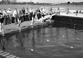 Bildserie från slutet av 1930-talet från Karlstads dåvarande simstadion. Anläggningen låg i anslutning till den s k badholmens östra sida söder om Kanikenäset. Badet invigdes 1923 och togs ur bruk och revs 1943 pga dålig vattenkvalité. En liknande konstruktion som ersatte den på bilderna  byggdes upp i Örsholmstjärnet i början av 1950-talet.
