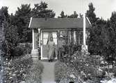En man och en kvinna vid en liten stuga i Kalmar södra koloniområde, fotograferat omkring 1930. Kalmar södra koloniförening grundades 1917 och har idag 105 kolonilotter. Området ligger strax söder om länssjukhuset i Kalmar med huvudingång från Stensbergsvägen.