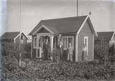 En stuga, två män och två kvinnor i Kalmar södra koloniområde, fotograferat omkring 1930. Kalmar södra koloniförening grundades 1917 och har idag 105 kolonilotter. Området ligger strax söder om länssjukhuset i Kalmar med huvudingång från Stensbergsvägen.