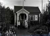 En stuga, man kvinna och tre barn i Kalmar södra koloniområde, fotograferat omkring 1930. Kalmar södra koloniförening grundades 1917 och har idag 105 kolonilotter. Området ligger strax söder om länssjukhuset i Kalmar med huvudingång från Stensbergsvägen.