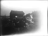 Troligen i Sikvik. Längst till vänster Ellen Olsson, en svägerska till Elna Brundin, därefter Anna Larsdotter Olsson (Elnas mor) och bakom henne David Brundin. Sören Brudin sitter tillsammans med mormodern Anna. Övriga barn Brundin i bakgrunden tillsammans med Einar Olsson och hans son Bengt. Bilden kan var från 1923-24.