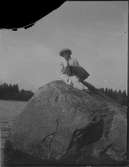 Elna Brundin sitter på en sten och spelar dragspel, antagligen i Harnäs, 1912-13.
