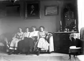 Systrarna Olsson, från vänster Naemi, Gertrud, Hanna och Elna. På fotot i bakgrunden tronar Lars Olsson, deras far. Fotot förmodligen taget hemma hos modern Anna Larsdotter Olsson.