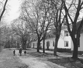 Tre bostäder tillhörande Gysinge bruk och Herrgården. Orangeriet är till vänster och personerna promenerar mot herrgården.