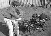 Pojke och liten flicka skjutsar en ännu mindre flicka i barnvagn. Familjen Taikons läger i Johanneshov, södra Stockholm.