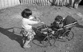 Liten flicka skjutsar en ännu mindre flicka i barnvagn. Familjen Taikons läger i Johanneshov, södra Stockholm.