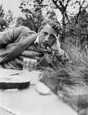 John Bauer ligger i gräset med pipan i munnen.