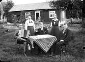 Fem personer i trädgården, en spelar dragspel. Från vänster: Halvar Stahre, Eda Stahre, Manne Sihlén, Hanna Sjökvist, född Stahre och Henning Sihlén.