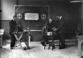 Interiör, tre män, varav två vid en fonograf.