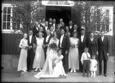 Rölanders bröllop. Gruppbild med bröllopsgäster på trappa framför hus. Brudparet i mitten.