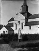 Kvinna poserar framför kyrka, platsen okänd.
